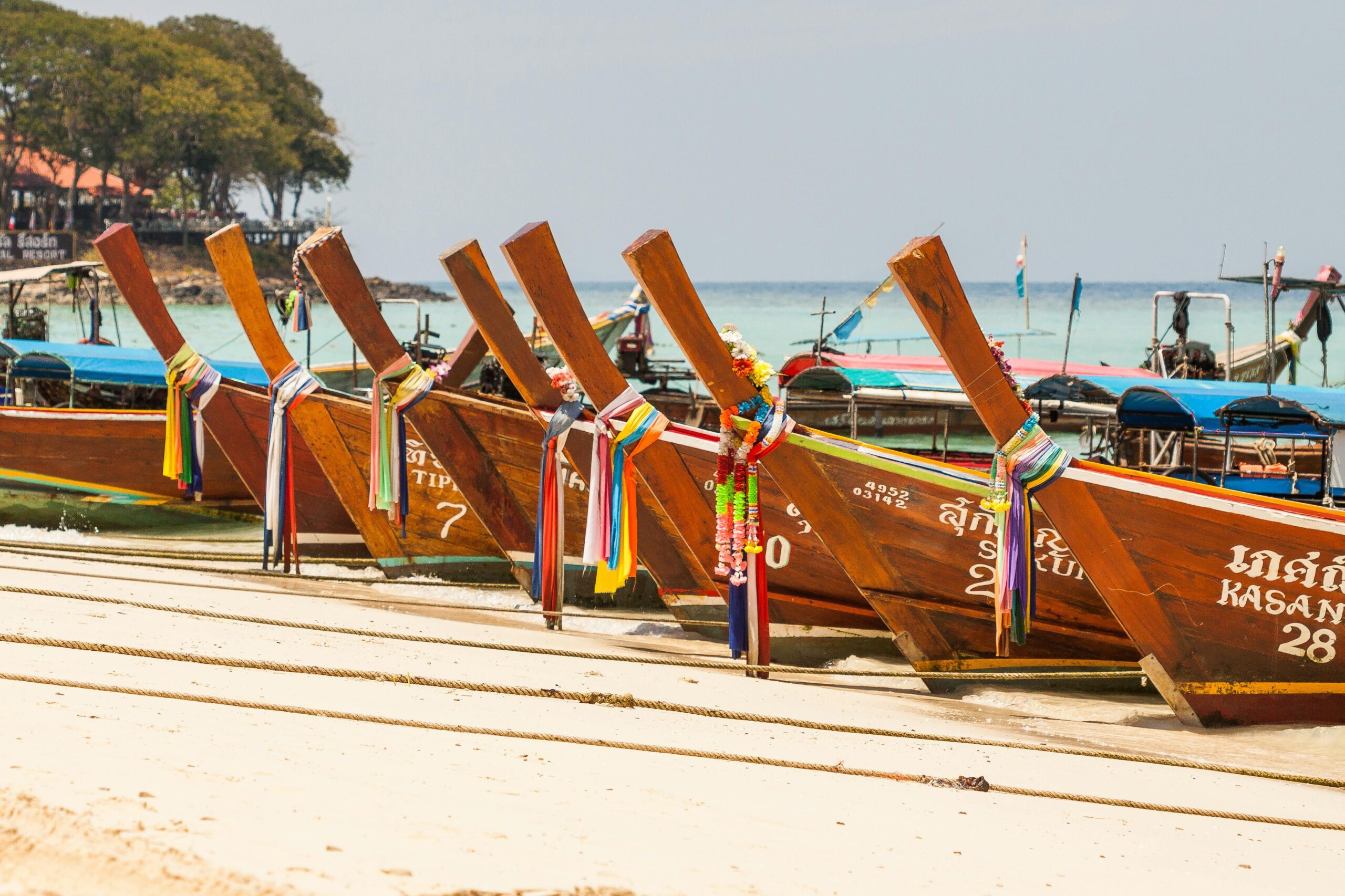 Home Vibrant longtail boats lined up on a sandy beach, perfect for travel and tourism imagery.